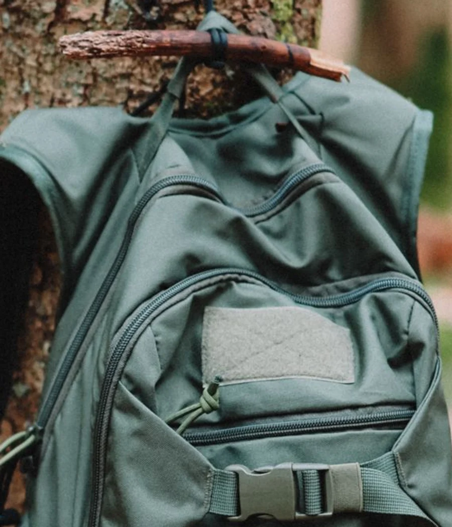 Upper pockets and straps of an olive hiking backpack hanging on a tree