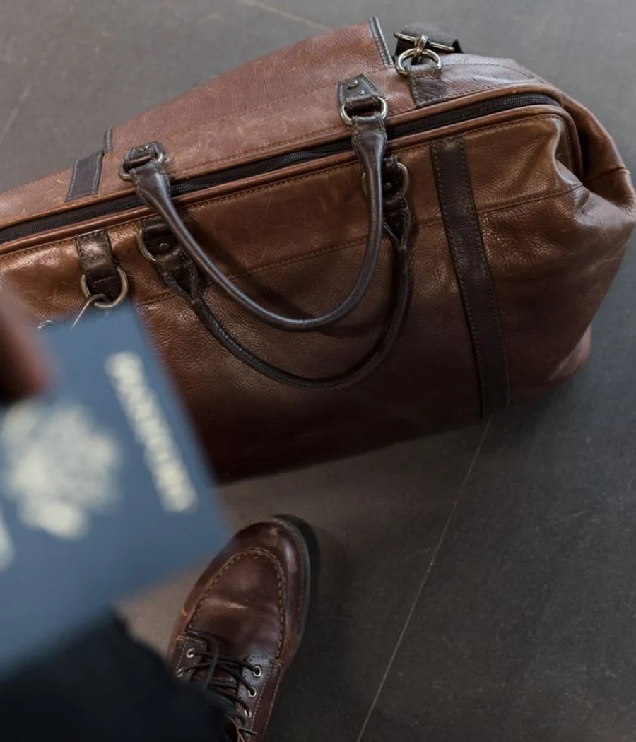 Brown leather weekender with handles and a shoulder strap on a tiled floor