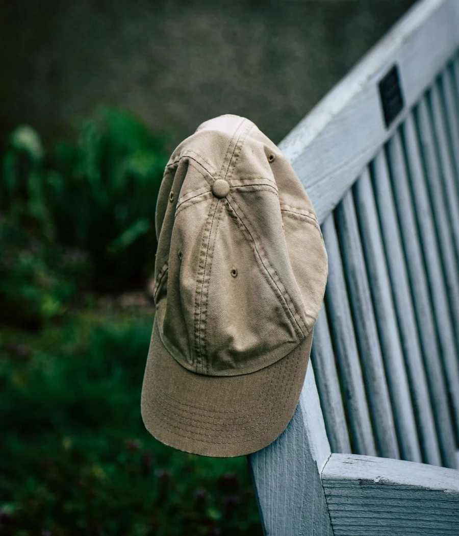 A plain sand-colored cotton cap hanging on a wooden bench