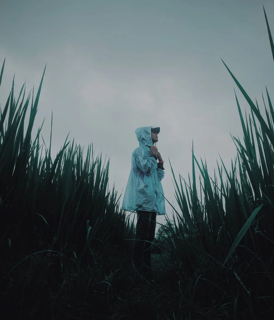 A person wearing a light hooded rain shell among tall grasses