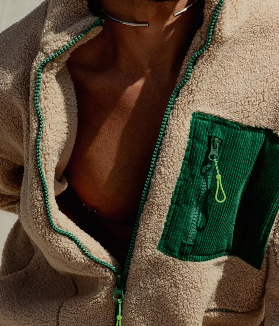 Detail of an oat-colored fleece jacket with a forest-green zip pocket