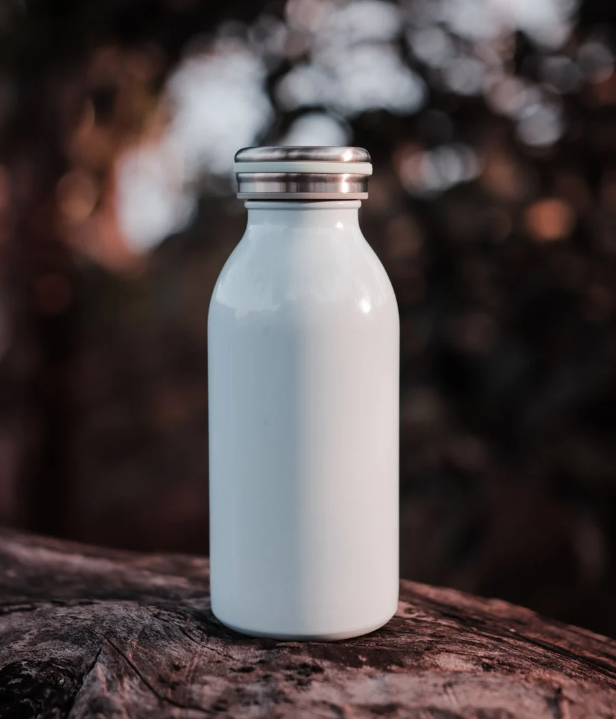A plain white metal trail bottle on a log in dappled light